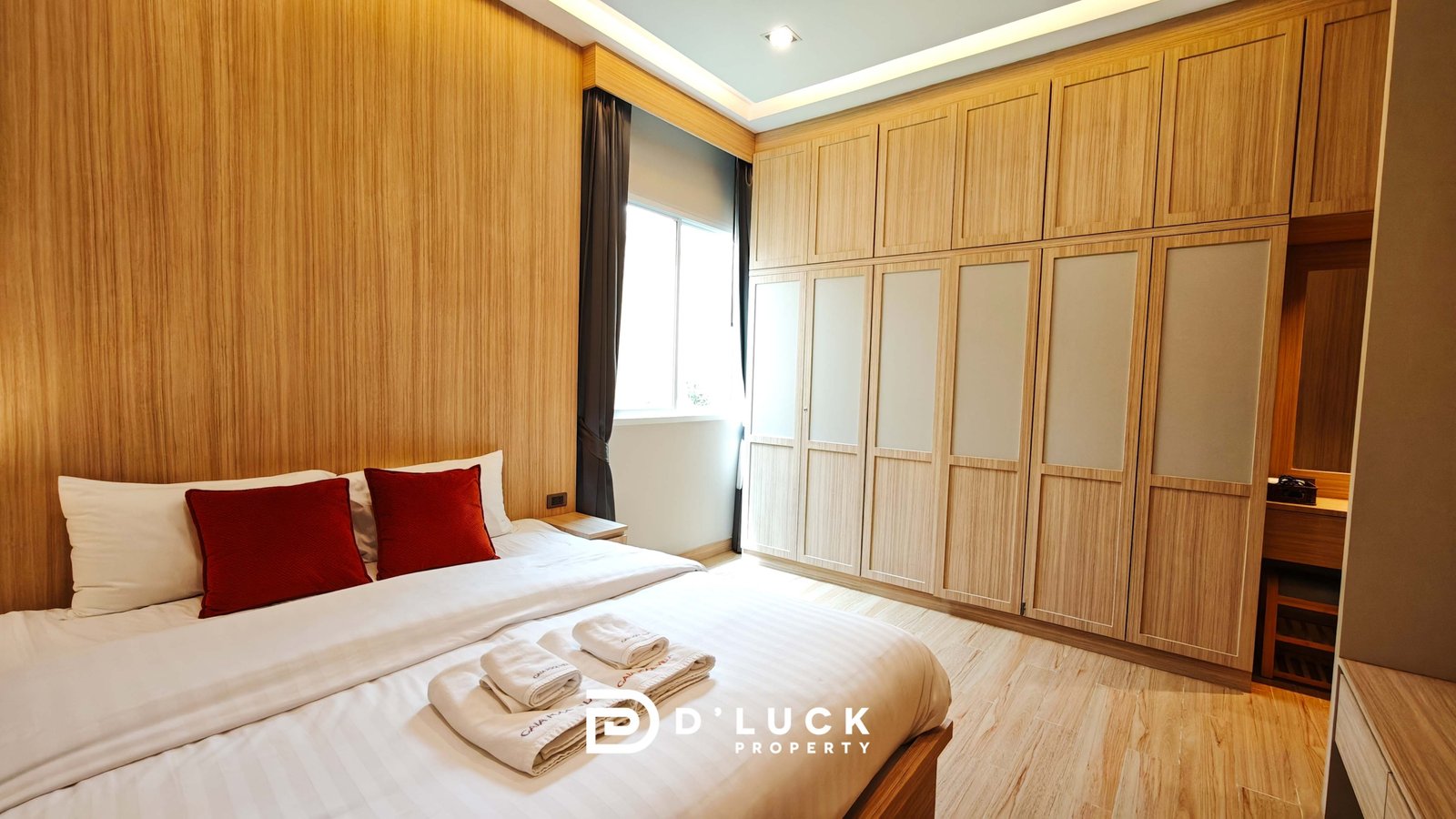 Hotel bedroom with two white beds and red pillows, wooden wall panels, and a large built-in wardrobe along the right wall.