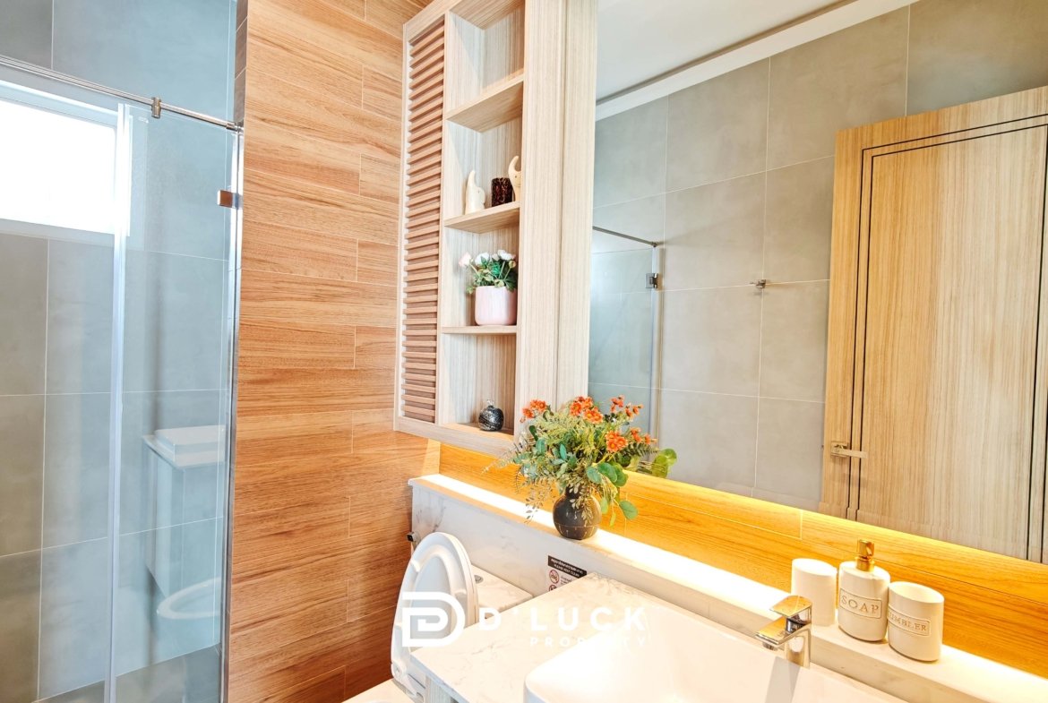 Modern bathroom with glass shower door, tan tiles, and a wooden shelving unit beside the sink