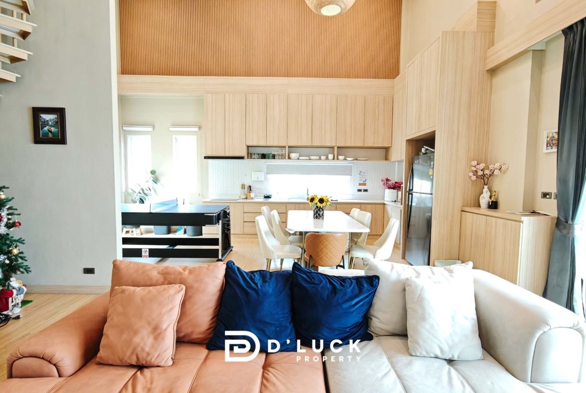 Open-plan living area with a Christmas tree, peach and navy cushions on a beige sofa, and light wood kitchen cabinets.