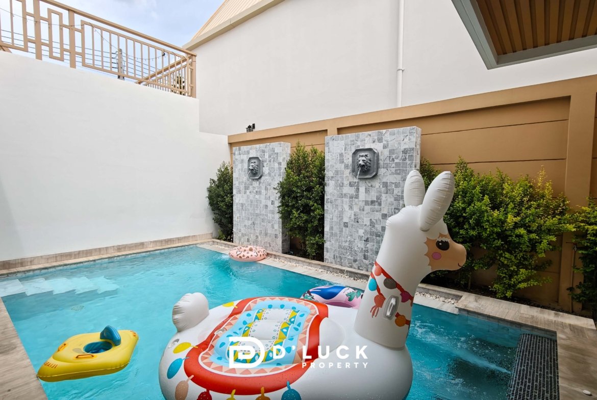 Pool in a courtyard with inflatable unicorn and yellow raft on blue water; decorative lion-head fountains on tiled stone columns and greenery nearby.