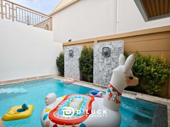 Pool in a courtyard with inflatable unicorn and yellow raft on blue water decorative lion head fountains on tiled stone columns and greenery nearby