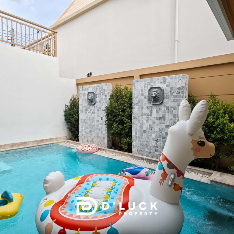 Pool in a courtyard with inflatable unicorn and yellow raft on blue water decorative lion head fountains on tiled stone columns and greenery nearby