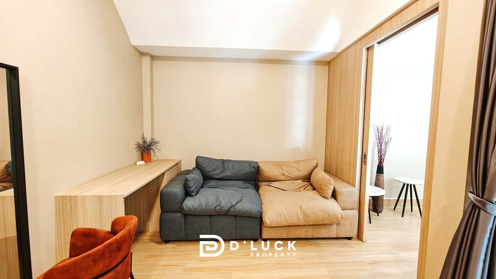 Cozy living room with beige walls, a two-tone sectional (gray and tan), a wooden desk along the left wall, and a sliding door on the right.