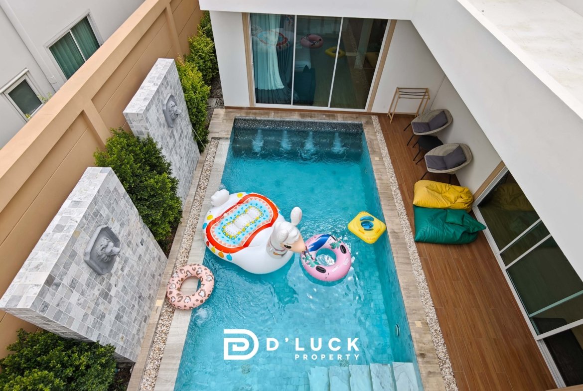 Top-down view of a rectangular pool in a private courtyard, with colorful inflatable floats and a wooden deck along the sides.