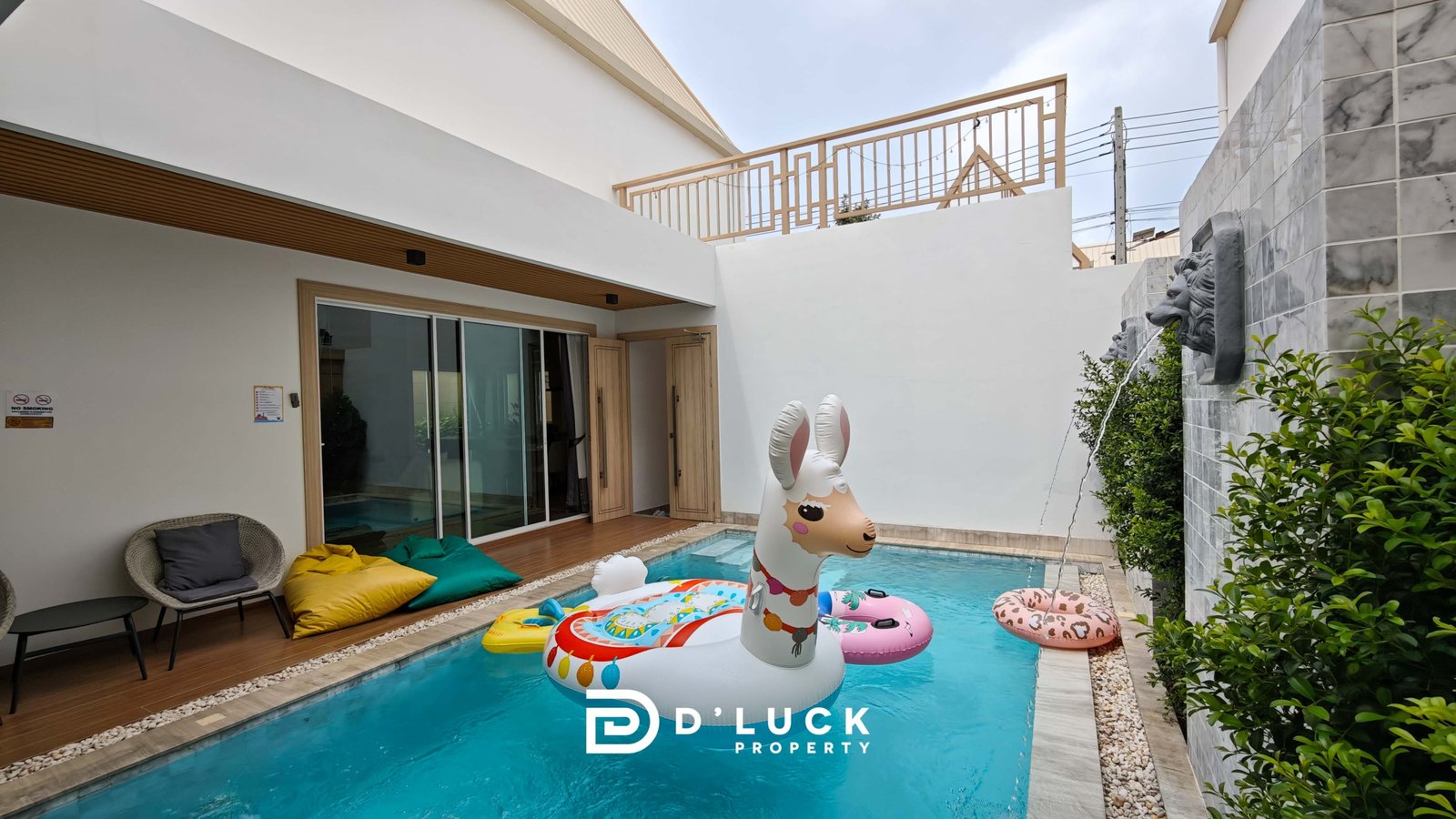 Pool area with inflatable animal floats (unicorn and flamingo) and colorful cushions by sliding glass doors.