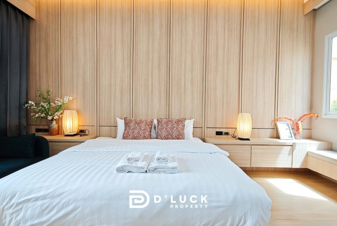 Modern hotel bedroom with a large wooden paneled headboard, white bedding, and matching lamps on both sides of the bed.