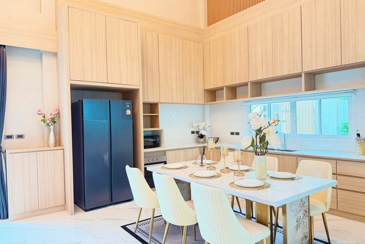 Bright open kitchen with light wood cabinets, a marble dining table set for six, gold candles, and white chairs; blue refrigerator on the left and flowers on the counter.