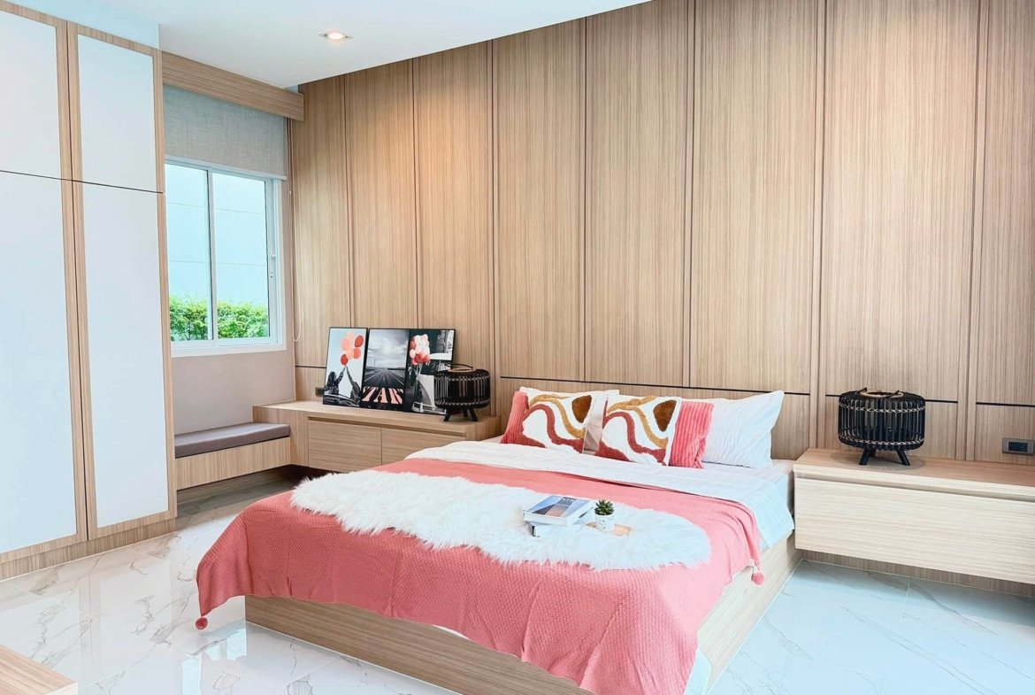 Modern bedroom with light wood paneling, platform bed in pink bedding and white fur throw, matching nightstands on each side