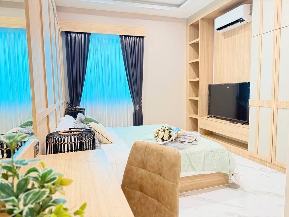 Modern hotel-style bedroom with a bed, wooden wall unit, TV, and blue curtains by a window with sheer panels.