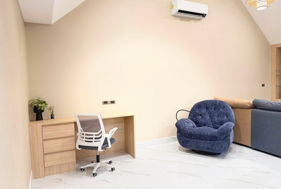 Home office corner with a wooden desk, white ergonomic chair, and a small potted plant on the left; beige walls and marble floor.