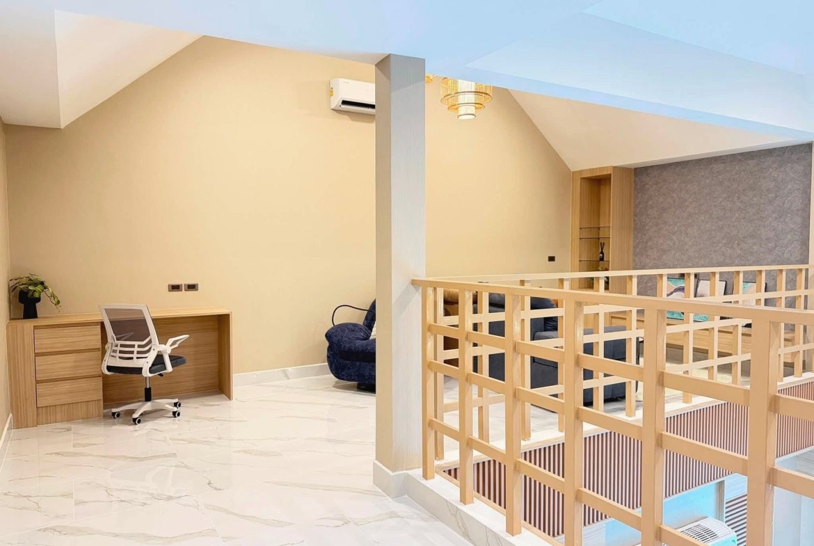 Open loft workspace with a wooden desk and white office chair against beige walls and marble floor, plant in corner, and railing dividing area.