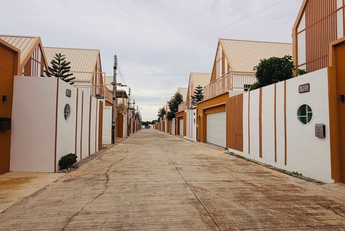 Row of modern, orange-and-white townhouses with slanted roofs along a paved street under a cloudy sky.