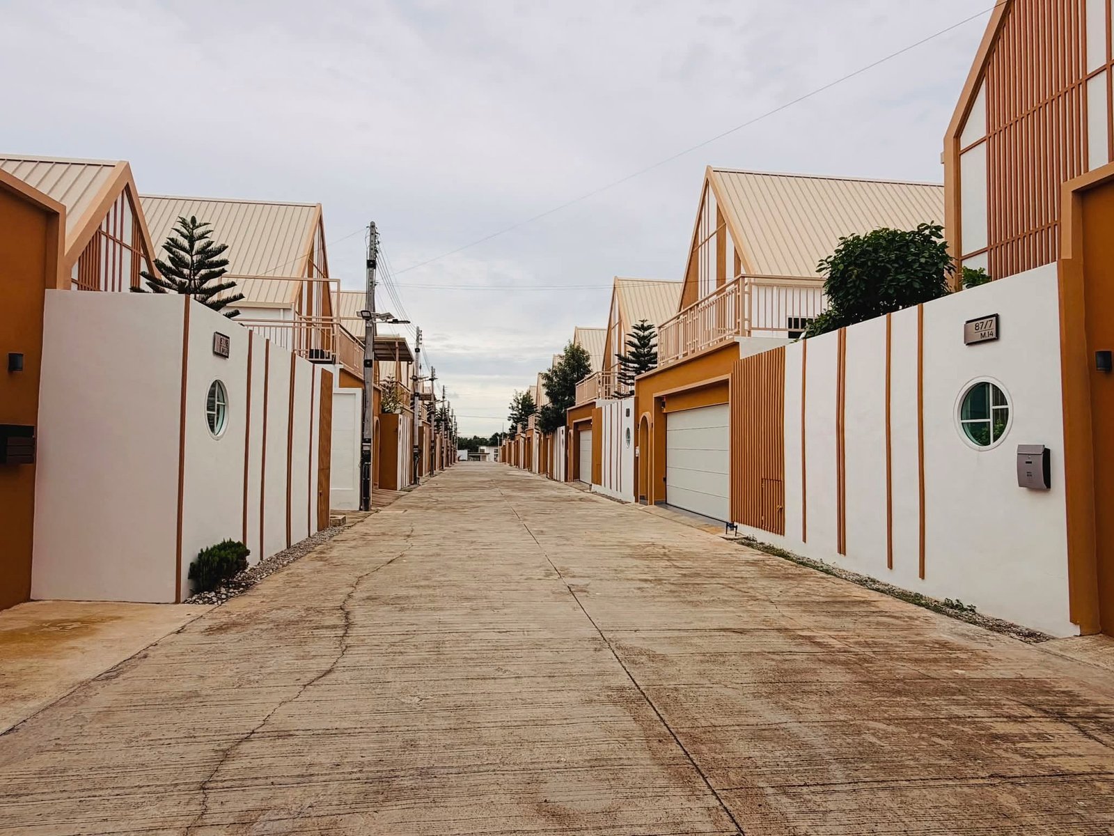 Narita_Villa_Pattaya_Rent_Rdl339_26 Row of modern, orange-and-white townhouses with slanted roofs along a paved street under a cloudy sky.