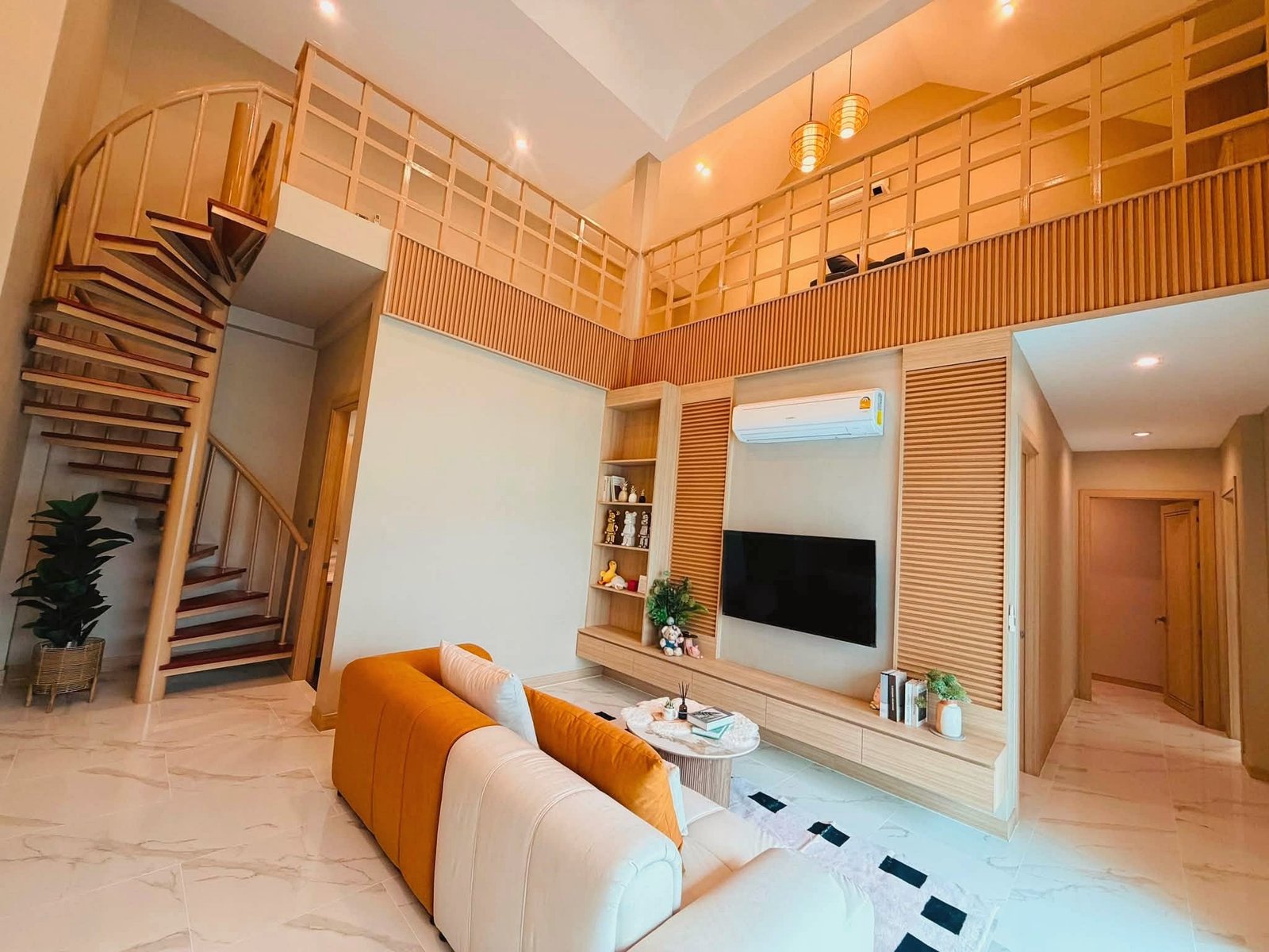 Narita_Villa_Pattaya_Rent_Rdl339_4 Open living room with orange and beige sectional, wall-mounted TV, and a wooden staircase leading to a mezzanine on the left.