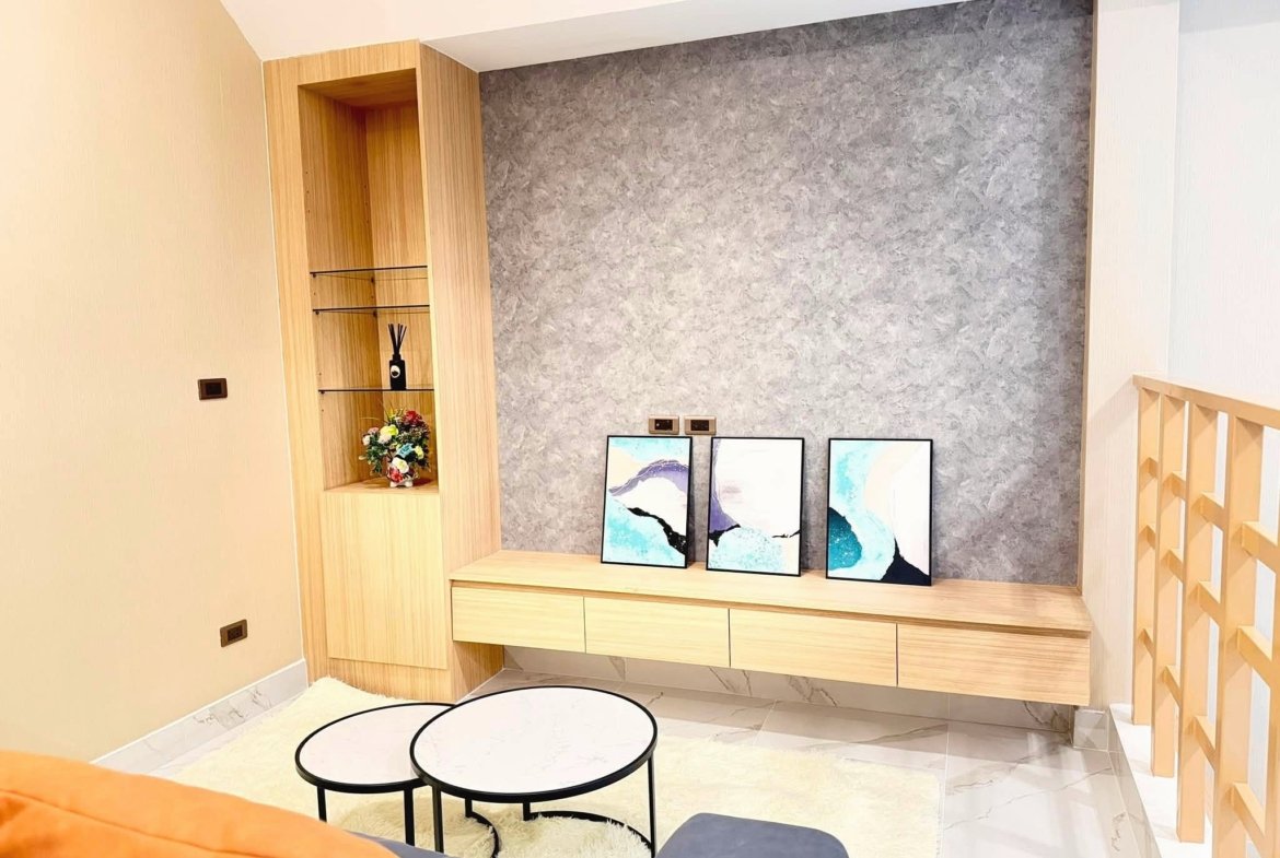 Modern living area with light wood built-in shelves, gray textured wall, and framed abstract paintings leaning on a console.