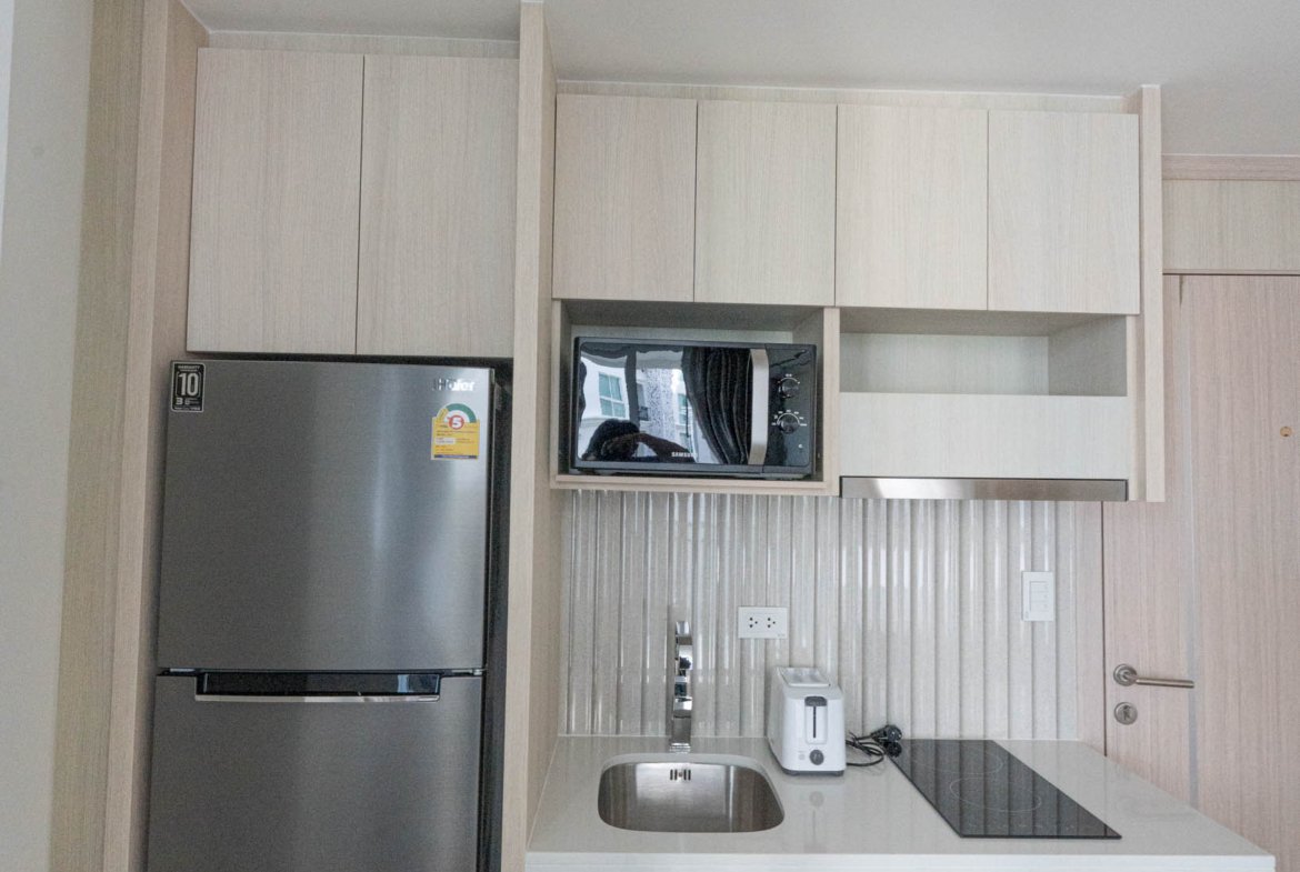 Modern kitchen with light wood cabinets, stainless steel fridge, built-in microwave, and white countertop.