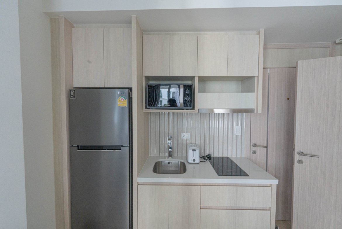 Modern light-wood kitchen with built-in microwave, tall fridge, and white countertop island.