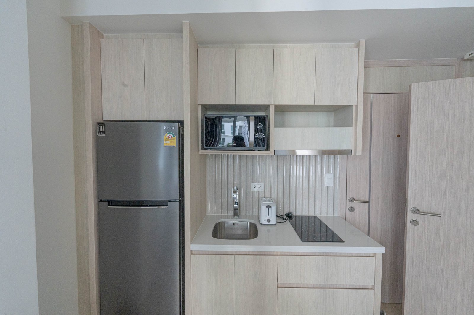 Olympus_C306_Rdl79A_9 Modern light-wood kitchen with built-in microwave, tall fridge, and white countertop island.