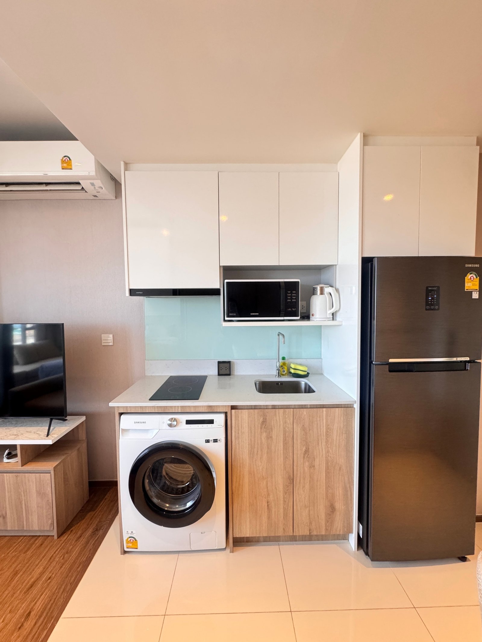 Once_Pattaya_1208_Rent_Rdl295_13 Modern compact kitchen with white upper cabinets, microwave on open shelf, kettle, and a stainless fridge to the right