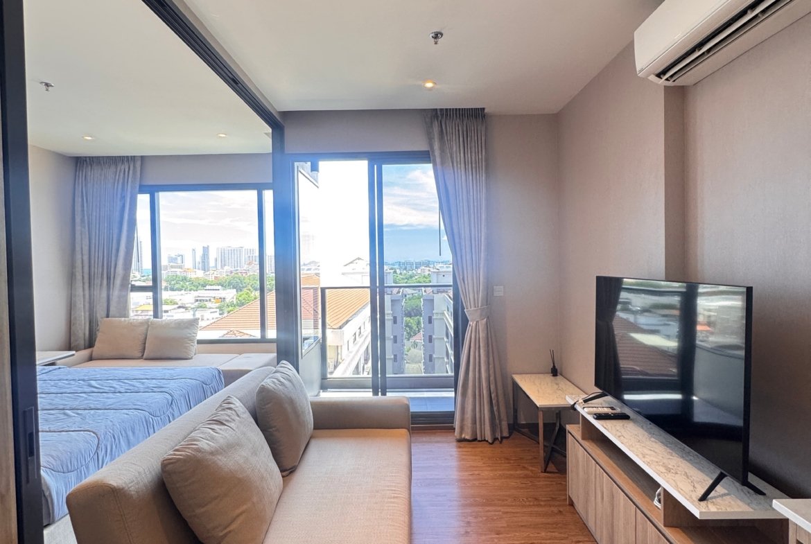 Modern living area in a high-rise apartment with a beige sofa, glass partition, and a city skyline visible through large windows.