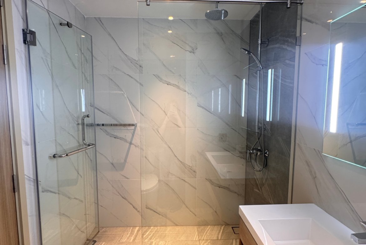 Modern bathroom featuring a glass shower enclosure with marble walls and a rainfall showerhead, plus a white rectangular sink and wooden vanity.