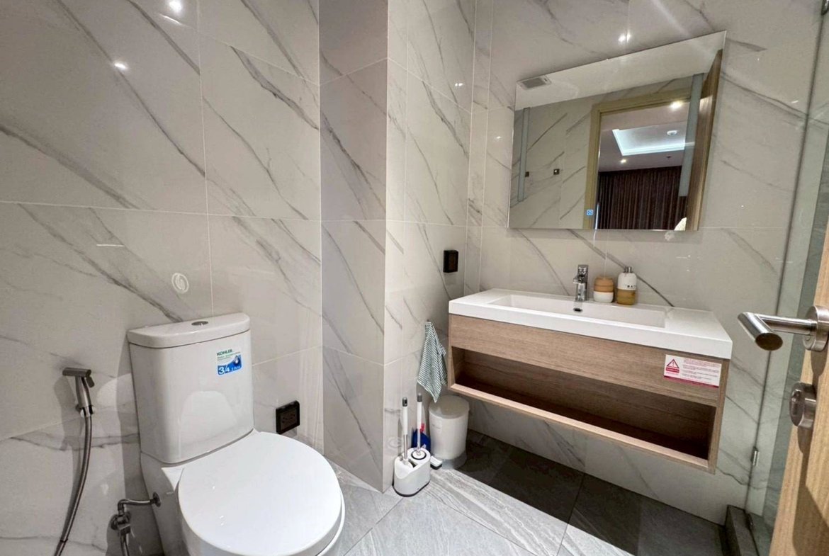 Modern marble-tiled bathroom with a white toilet, wall-mounted sink, and large mirror above the vanity.