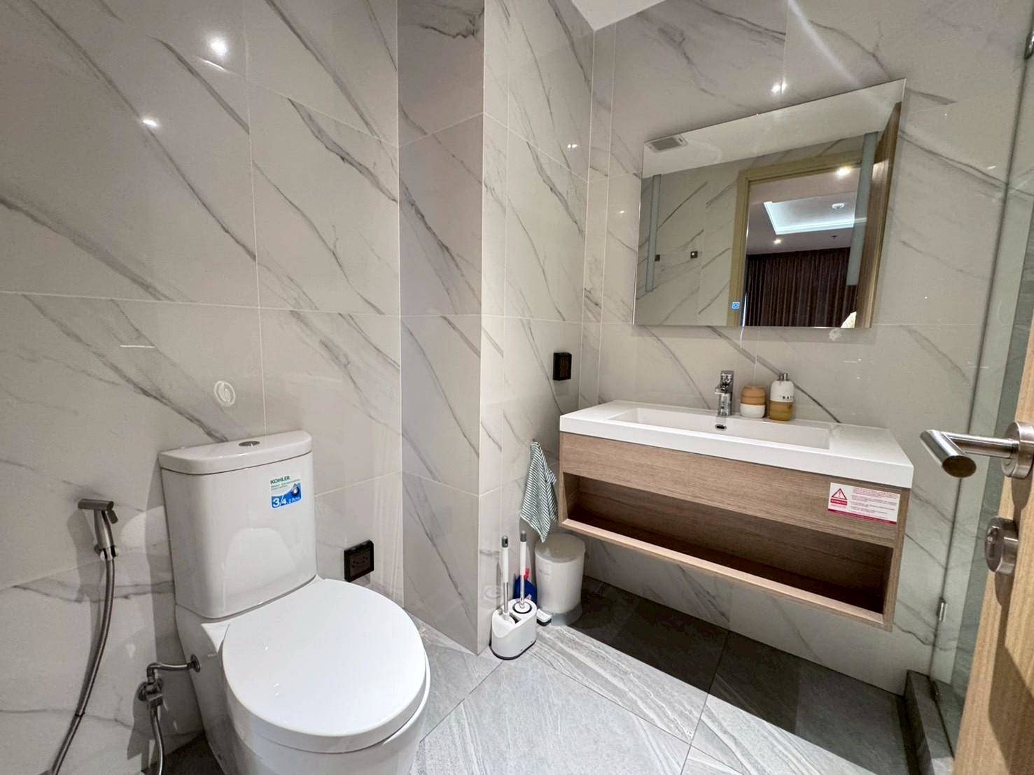Modern marble-tiled bathroom with a white toilet, wall-mounted sink, and large mirror above the vanity.