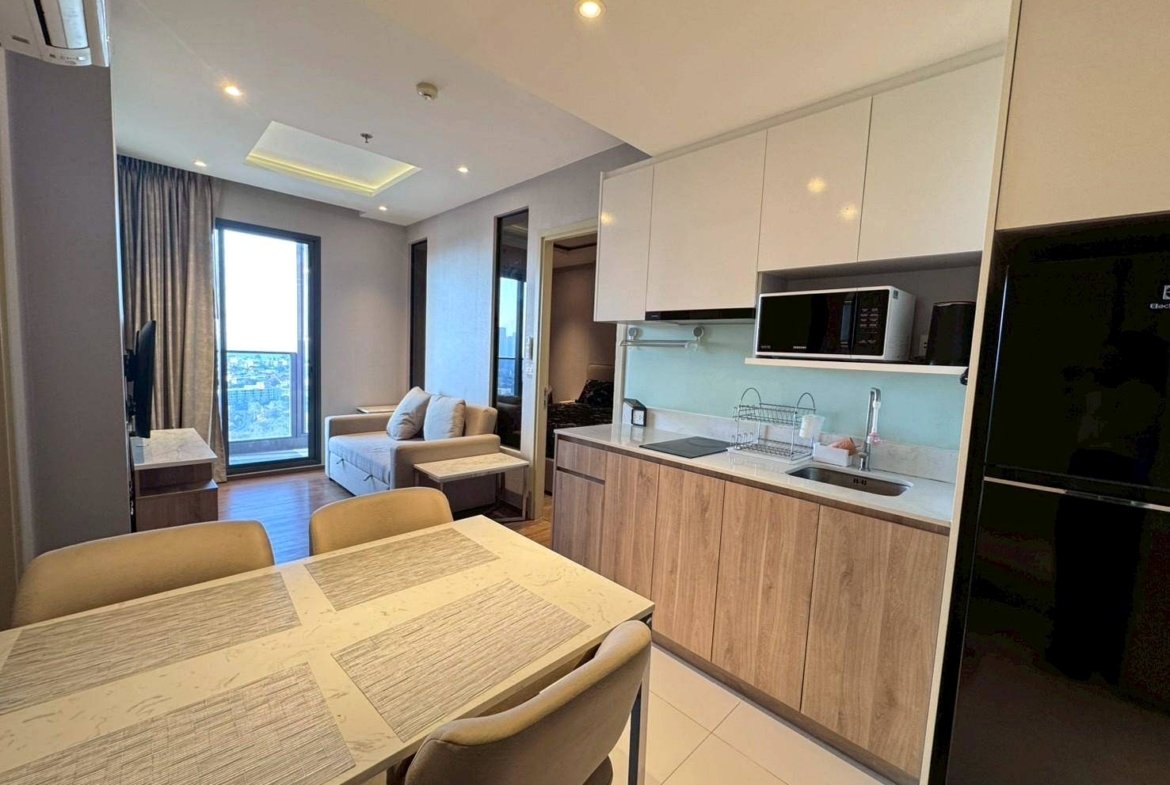 Open-plan kitchen and dining area with white upper cabinets, wood lower cabinets, a microwave, and a dining table in the foreground.
