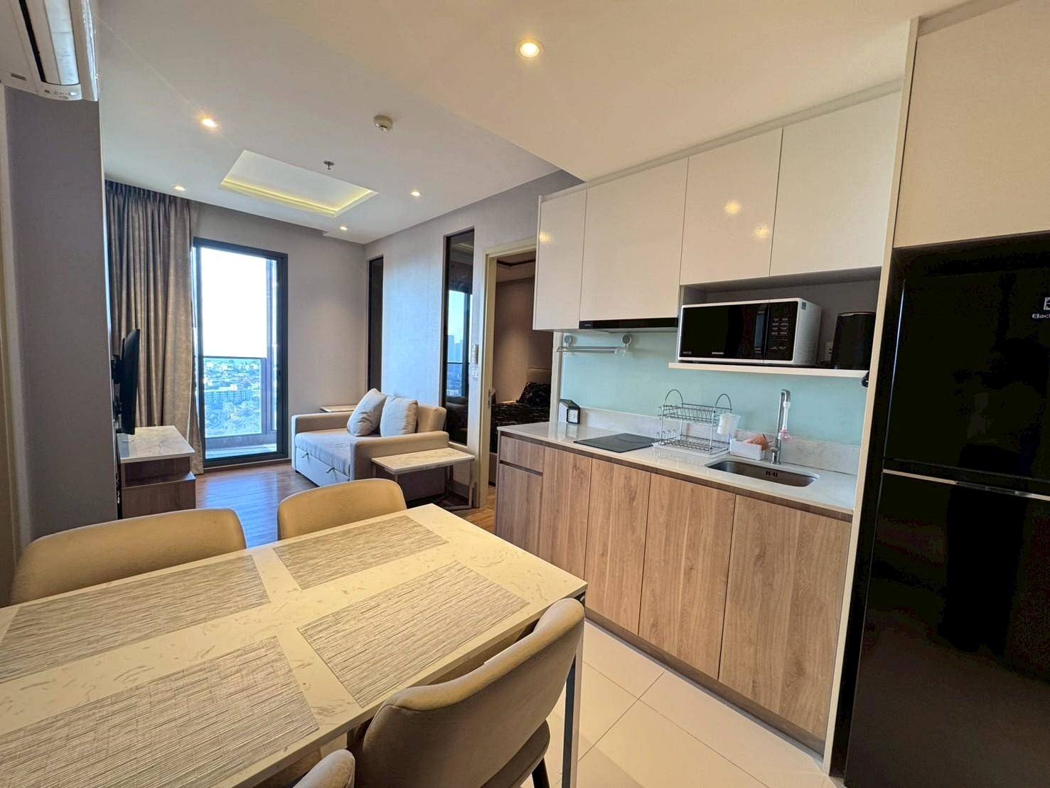 Open-plan kitchen and dining area with white upper cabinets, wood lower cabinets, a microwave, and a dining table in the foreground.