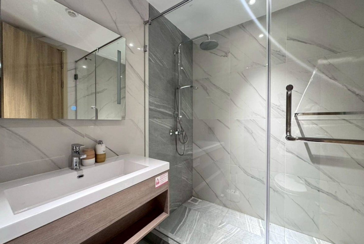 Contemporary bathroom with marble walls, glass shower enclosure, and wall-mounted sink.