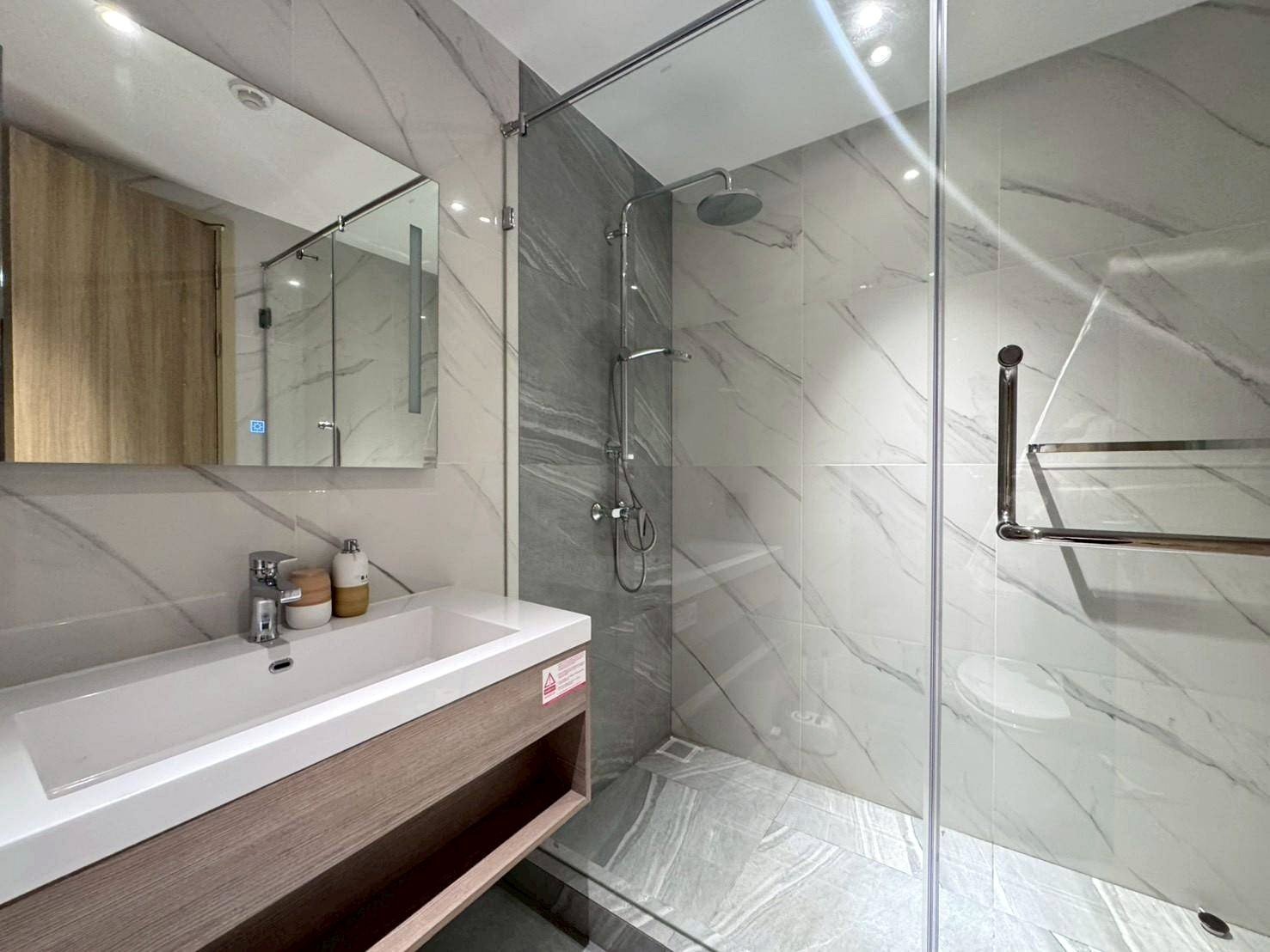 Contemporary bathroom with marble walls, glass shower enclosure, and wall-mounted sink.