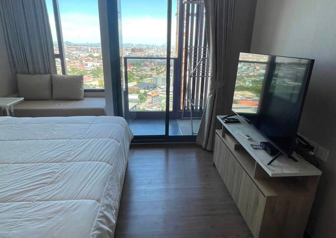 Hotel room with a white quilted bed, large glass doors to a balcony, and a city skyline view.