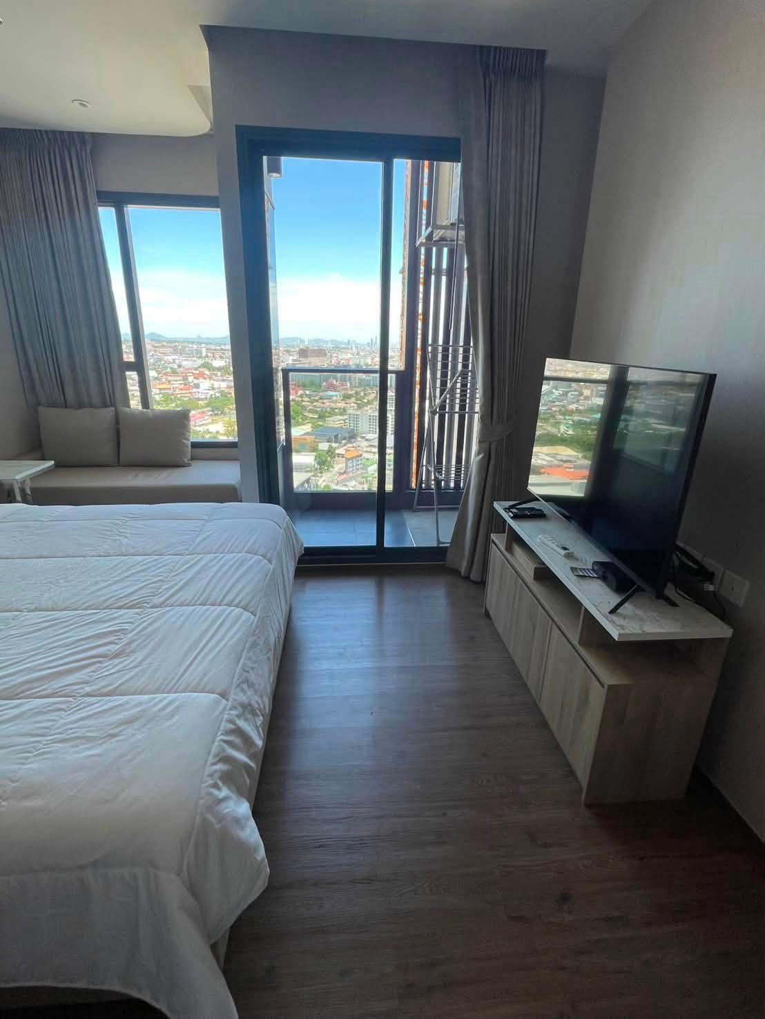 Hotel room with a white quilted bed, large glass doors to a balcony, and a city skyline view.