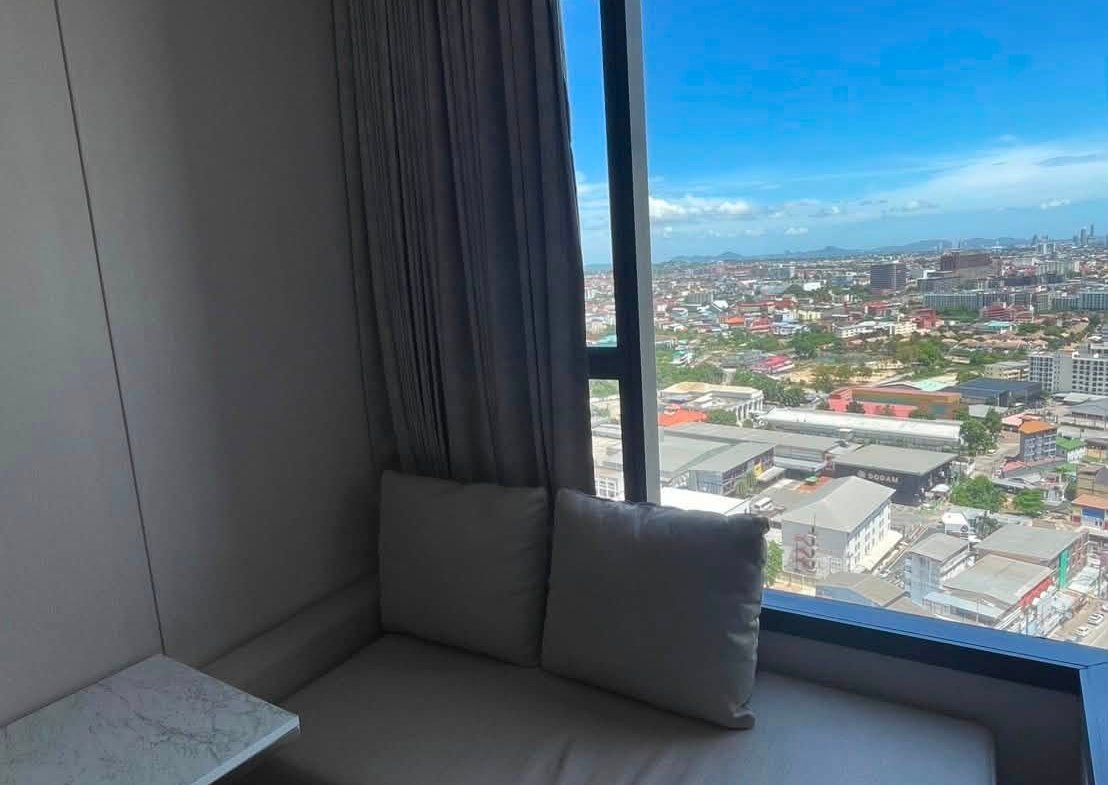 Gray cushioned window nook with a marble side table, overlooking a cityscape on a sunny day.