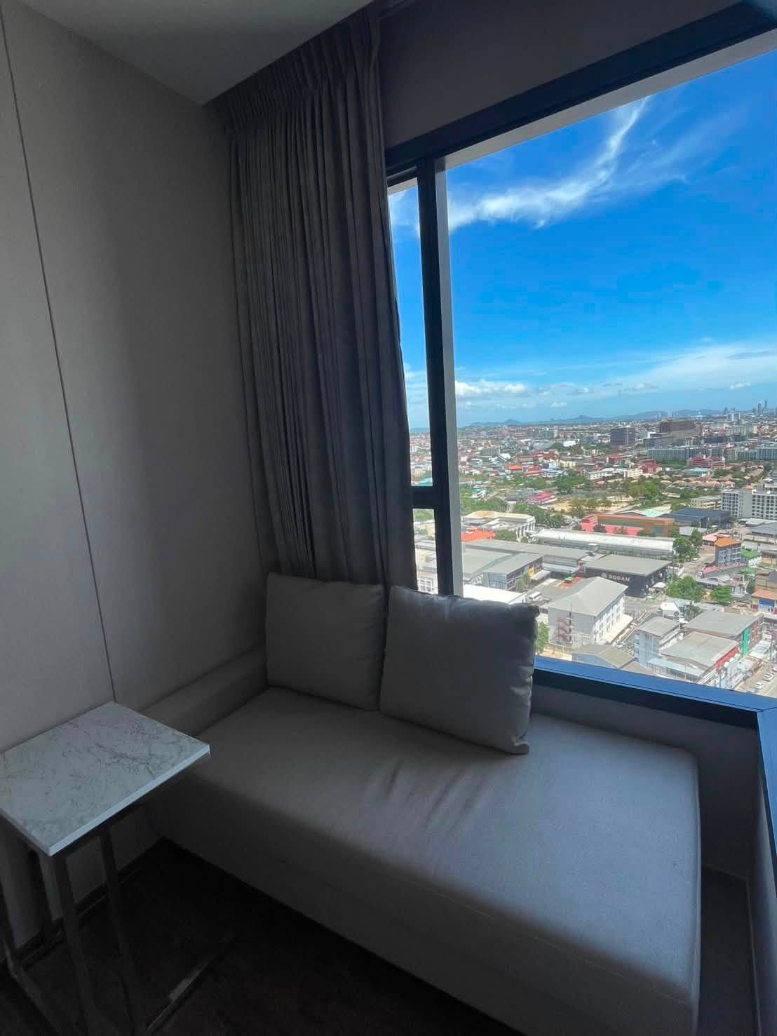 Gray cushioned window nook with a marble side table, overlooking a cityscape on a sunny day.