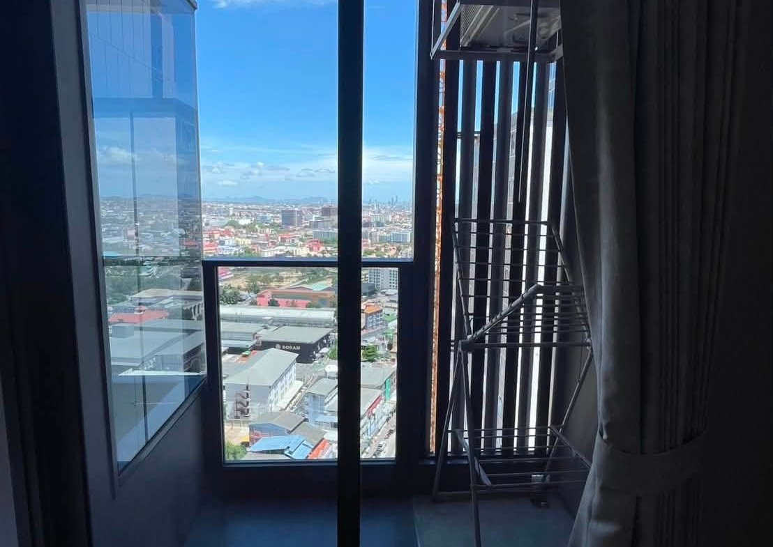 Indoor room with large glass balcony doors opening to a city view and blue sky; a metal drying rack is near the window.