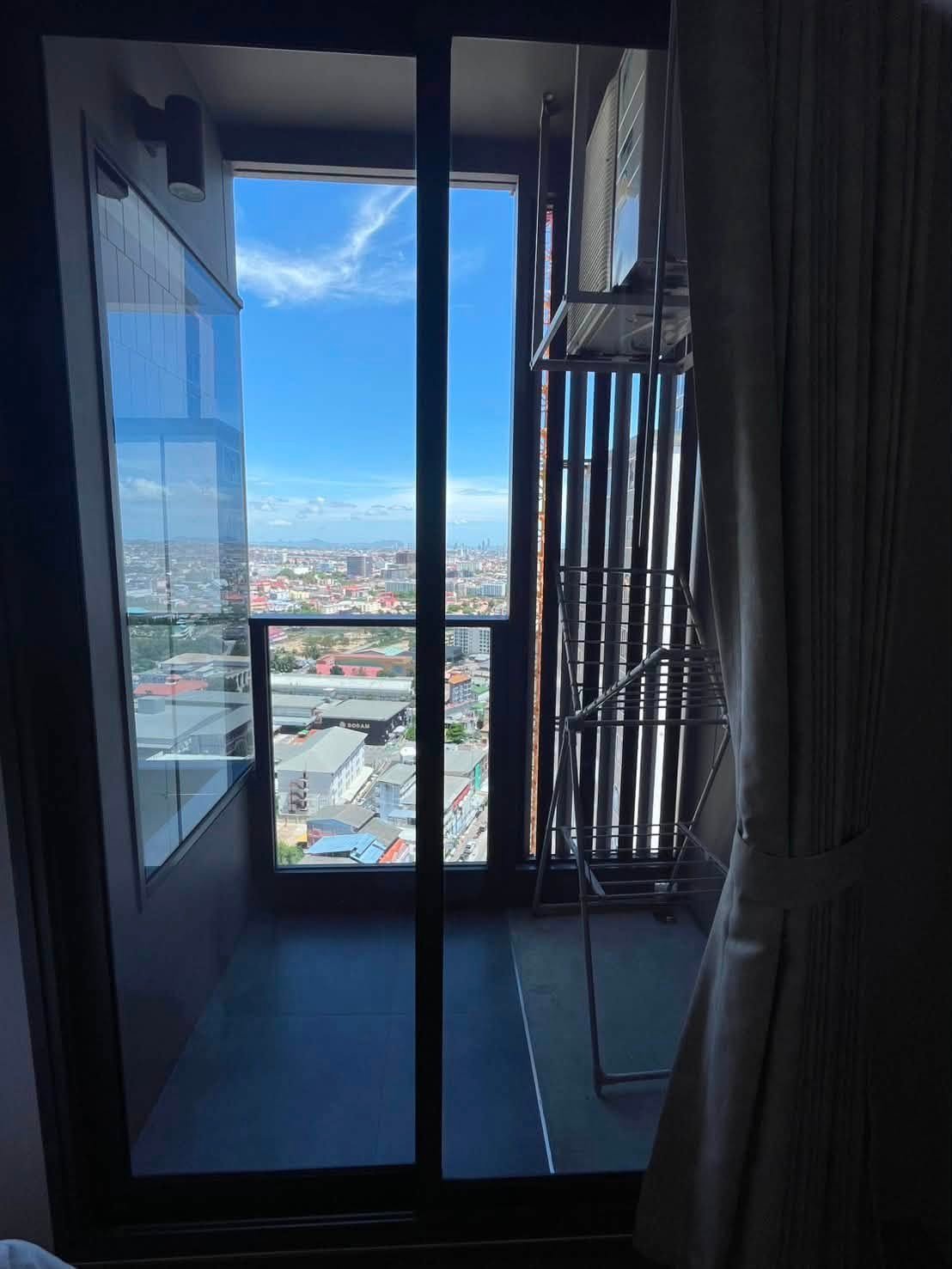Indoor room with large glass balcony doors opening to a city view and blue sky; a metal drying rack is near the window.