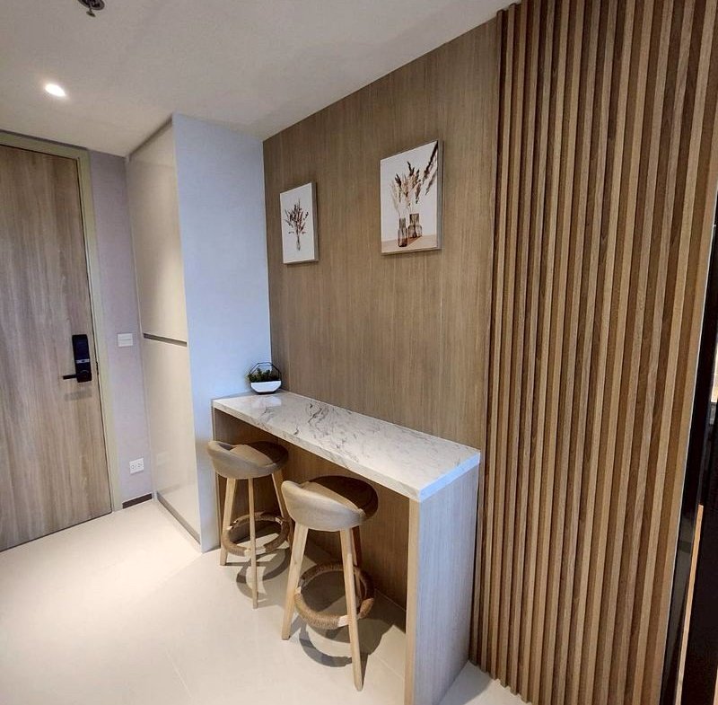 Minimalist entry area with a marble-topped counter, two wooden bar stools, a plant, and botanical prints on a wood-paneled wall with vertical slats.