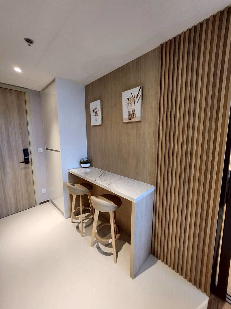 Minimalist entry area with a marble-topped counter, two wooden bar stools, a plant, and botanical prints on a wood-paneled wall with vertical slats.