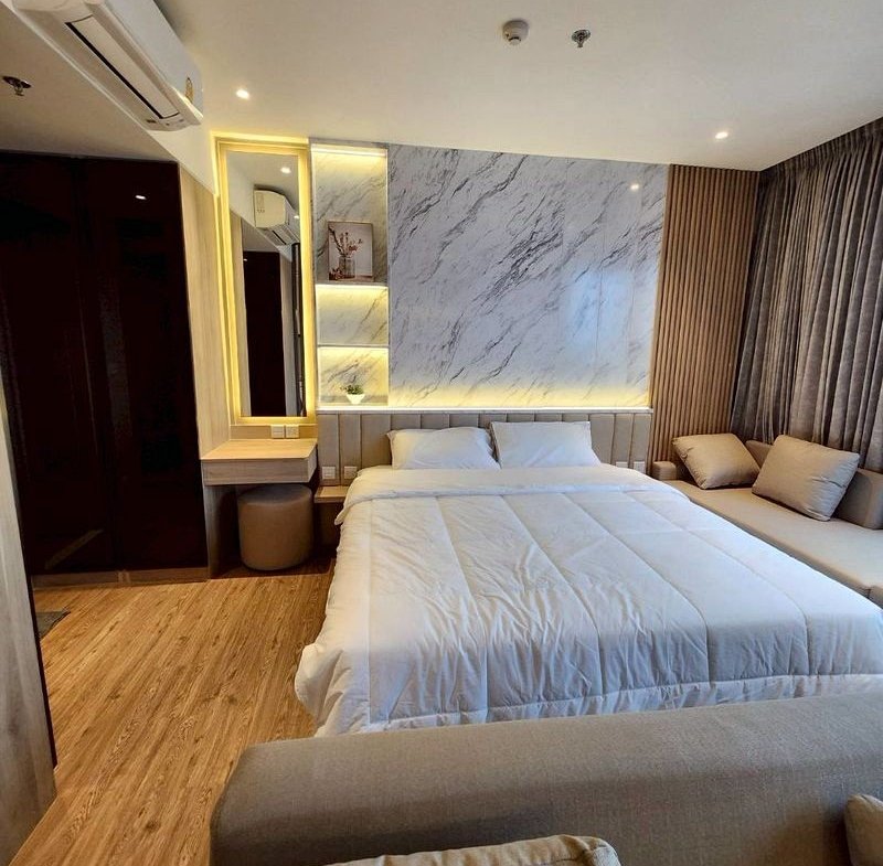 Modern hotel room with a large bed in white bedding, a marble accent wall, and a gray sofa seating area beside it.