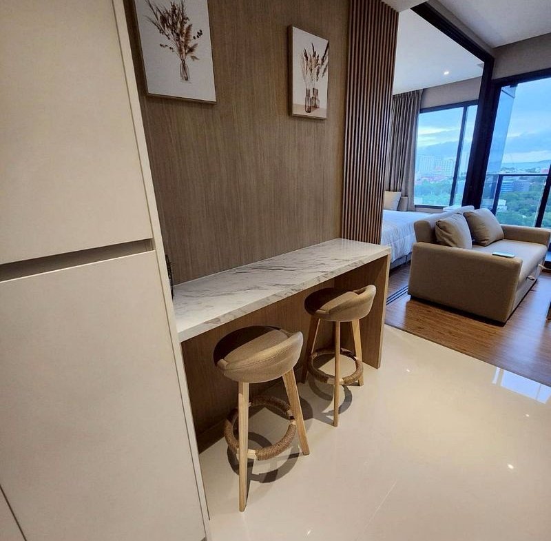 Modern hotel kitchenette with marble countertop and two wooden stools against a wood-paneled wall.