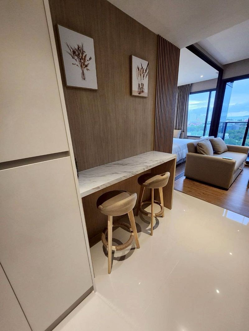 Modern hotel kitchenette with marble countertop and two wooden stools against a wood-paneled wall.