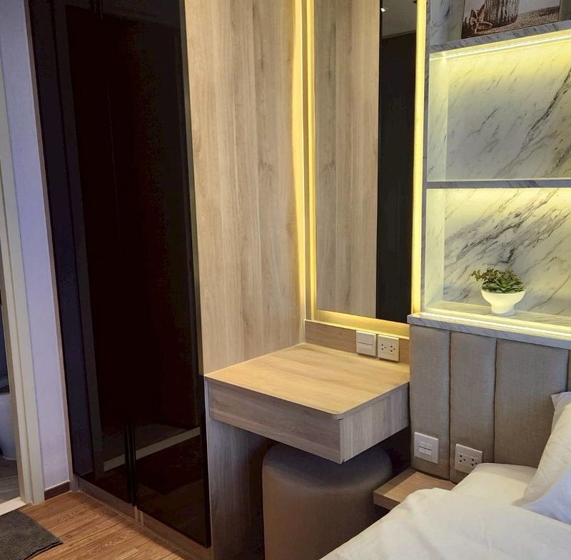 Modern bedroom with a tall black wardrobe, wood-paneled wall, and a backlit mirror above a floating desk near the bed.