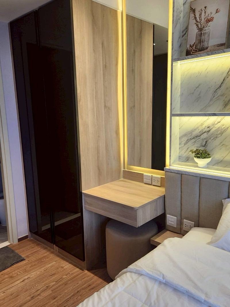 Modern bedroom with a tall black wardrobe, wood-paneled wall, and a backlit mirror above a floating desk near the bed.