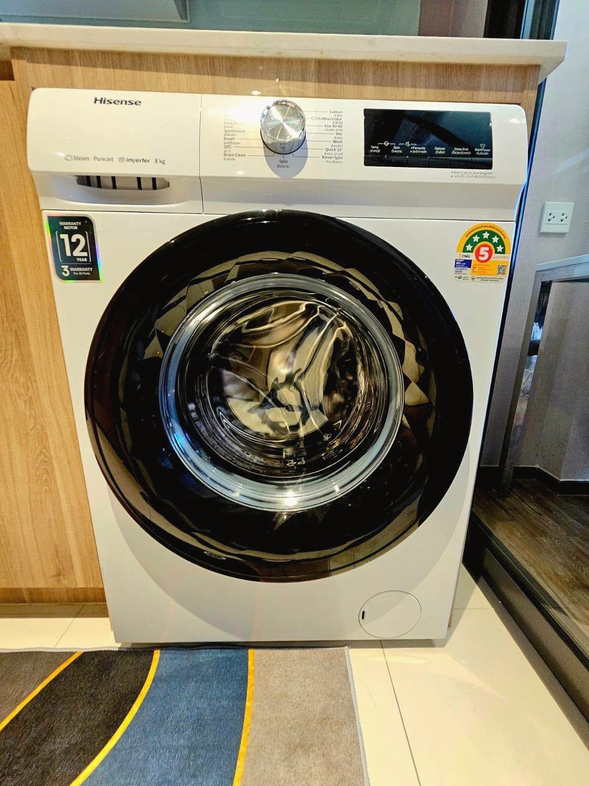 Once_Pattaya_Rent_Rdl337_11 White Hisense front-loading washing machine with large circular door and control panel on top, in a showroom setting.