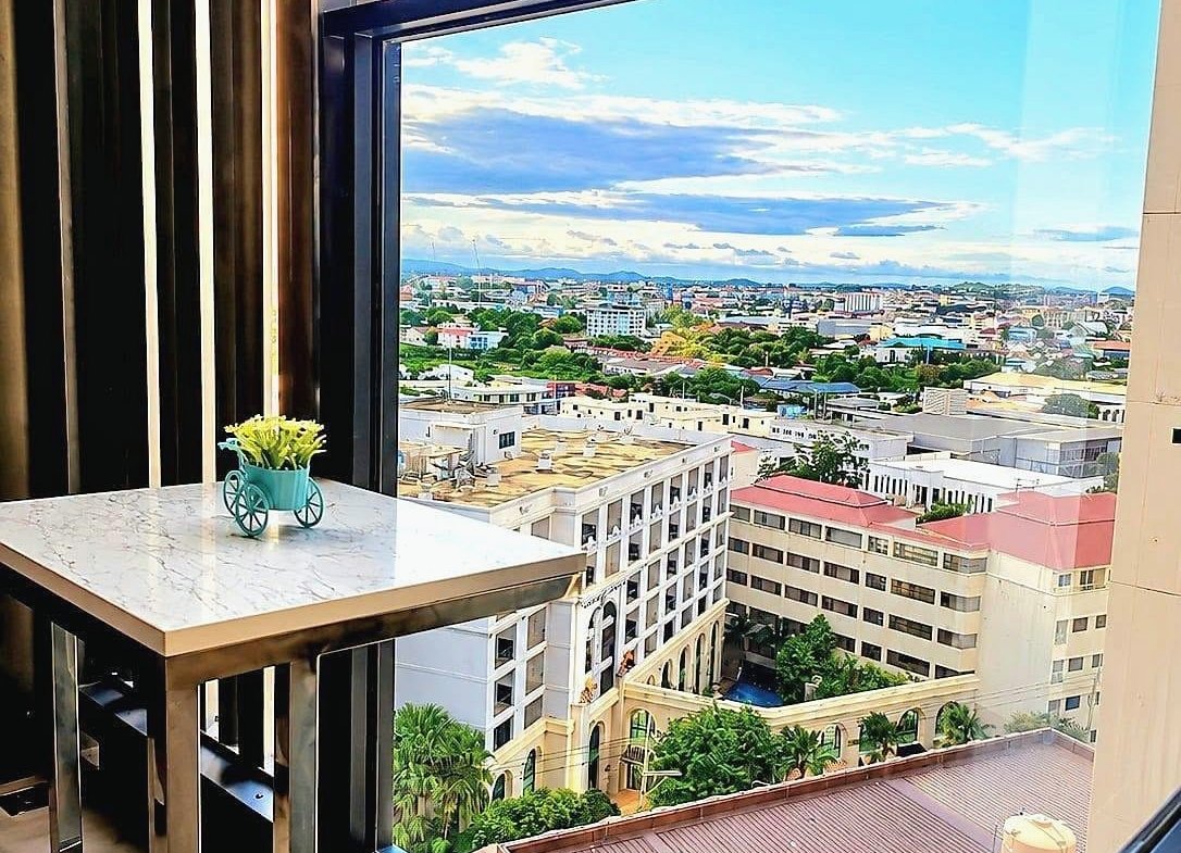 Marble-topped balcony table with a small turquoise plant in a decorative wheelbarrow-style pot, overlooking a cityscape and blue sky.