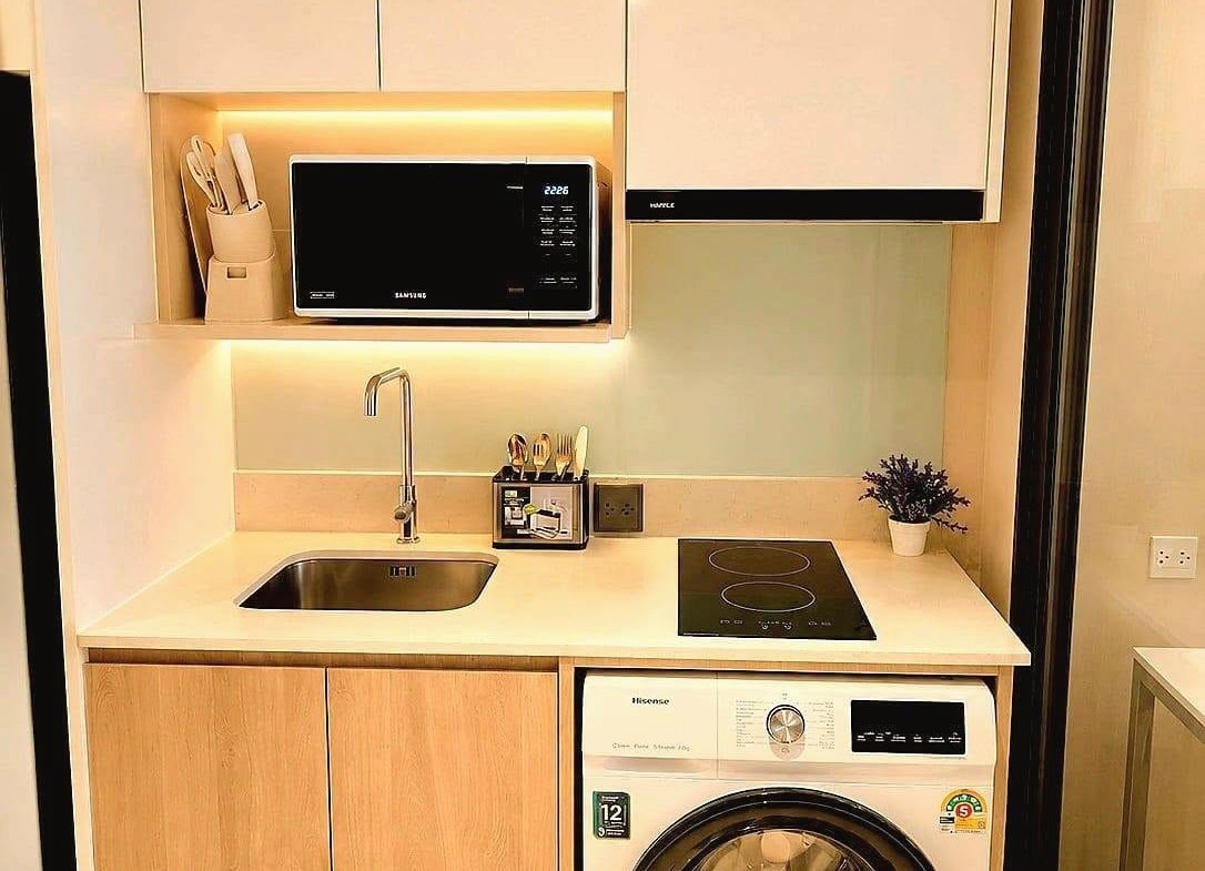 Compact kitchen with washing machine under the counter, induction hob, sink, and white upper cabinets with under-cabinet lighting.