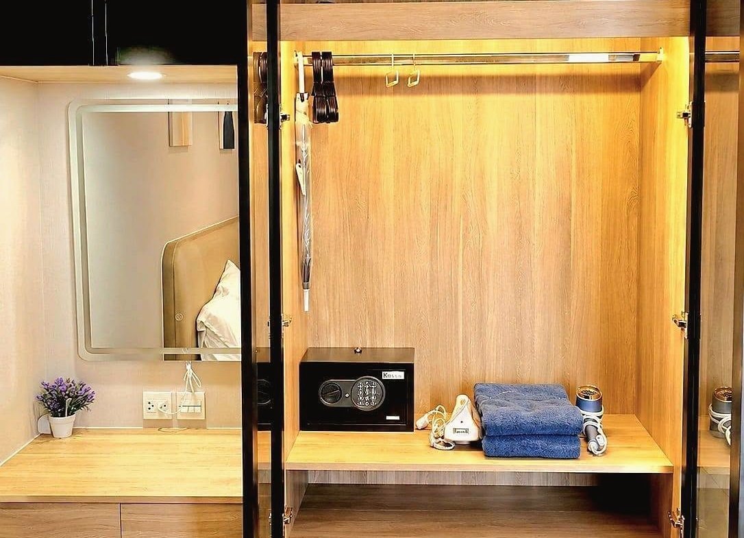 Open wooden wardrobe with clothes rail and built-in safe; on the shelf: folded blue towels, a hair dryer, and a small safe keypad.