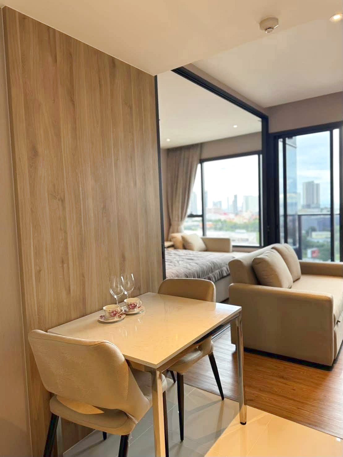 Once_Pattaya_Rent_Rdl366_11 Dining table for two with teacups and glasses in a modern suite, wood-paneled wall and open living area with city views.