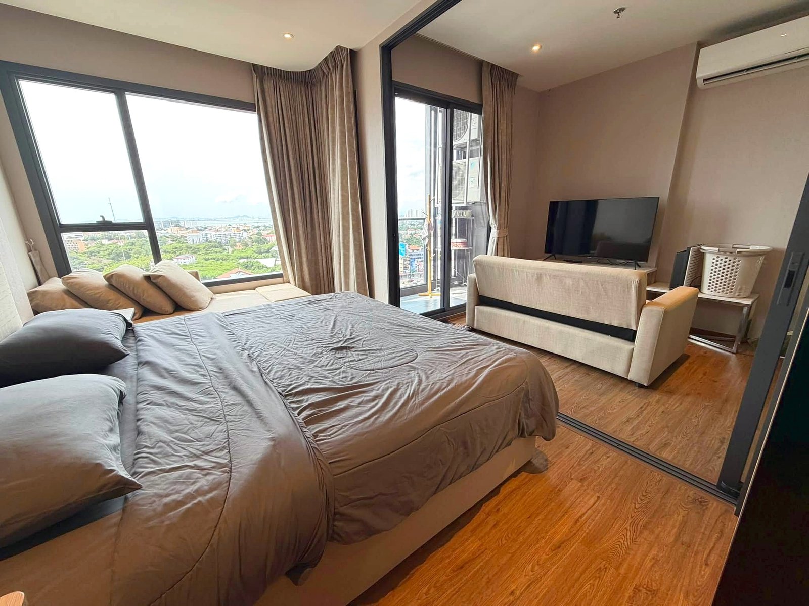Once_Pattaya_Rent_Rdl366_2 Bedroom with two full beds in brown bedding, beige sofa, and a wall-mounted TV; large windows reveal a city view in a high-rise apartment.
